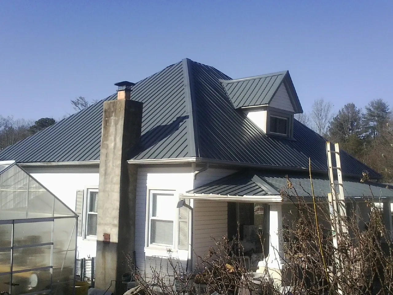 Dark blue standing seam metal roof on a white farmhouse with dormer — Slate & Tile Roof Repair by Roofing Brothers in Eldred