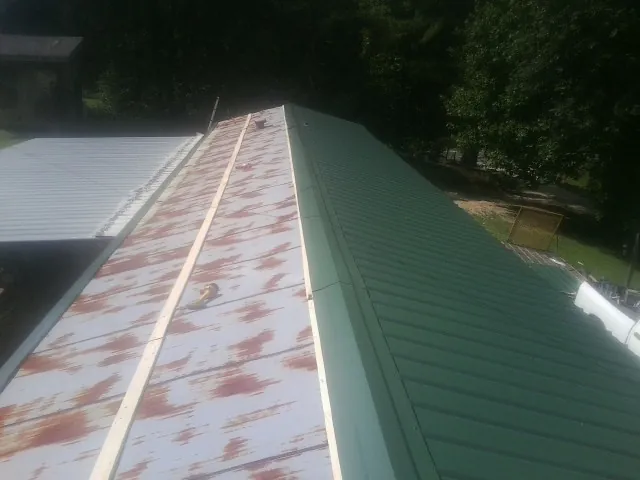 Old rusted panels beside newly installed green metal roofing — Wind Damage Roof Repair by Roofing Brothers in Eldred