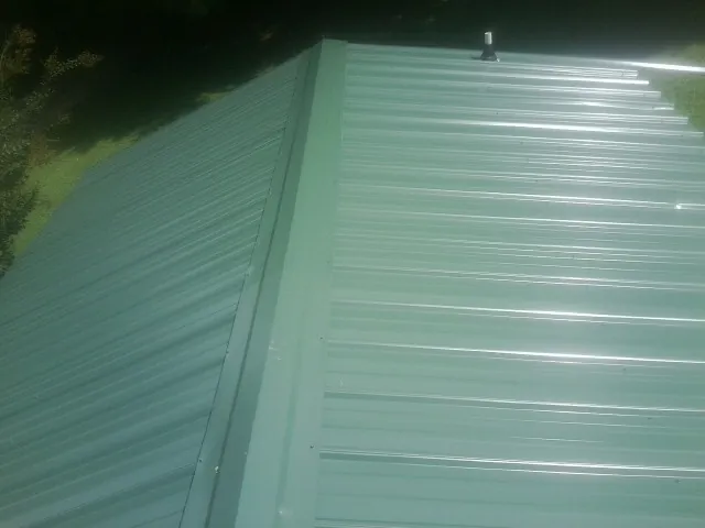 New green metal panels meeting at the ridge of a roof — Flat Roof Repair work by our crew in Eldred