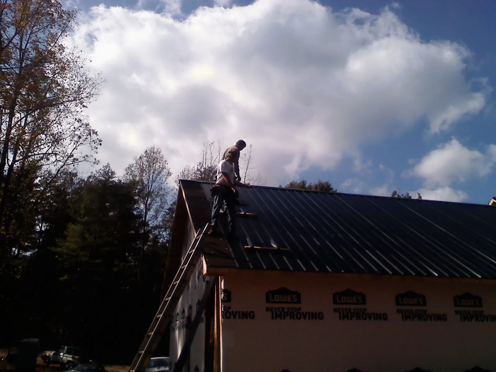 Roofer fastening dark metal panels high against a cloudy sky, from a Roof Inspection job in Eldred