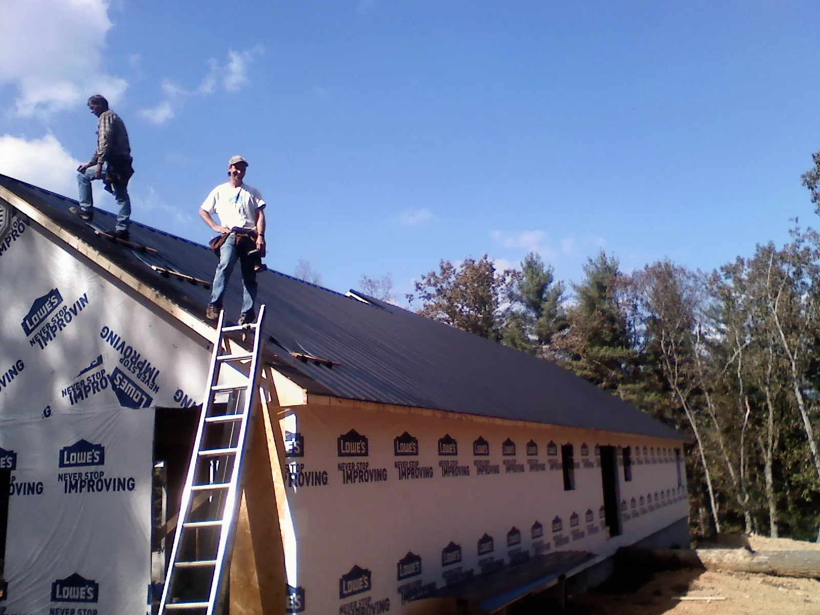 Two roofers standing on a long dark metal roof over a wrapped building in Eldred